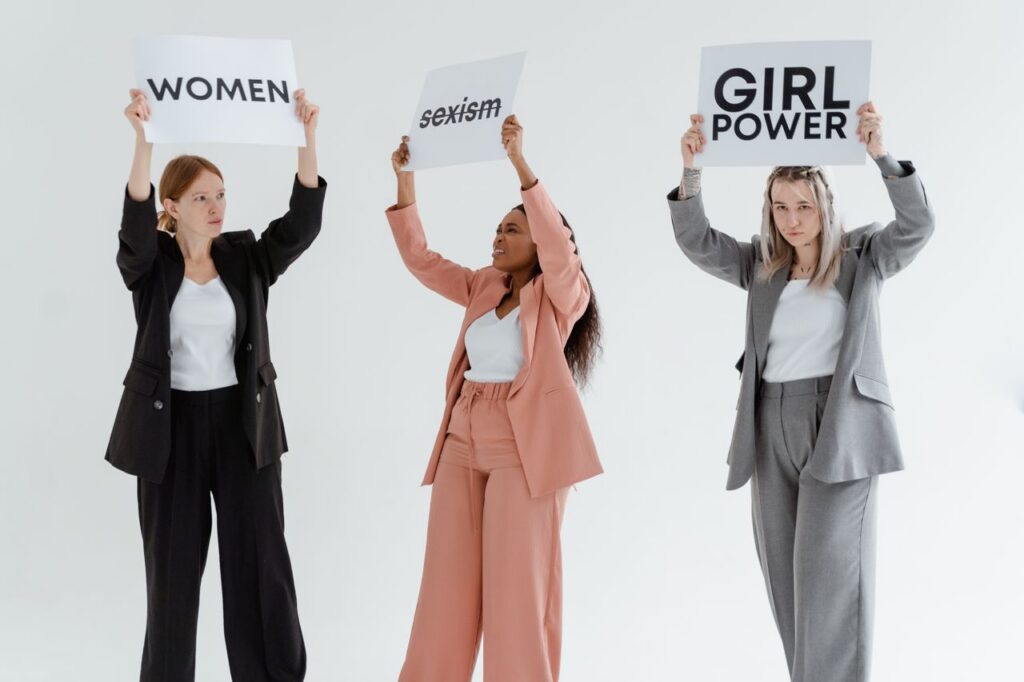 Three women in business attire holding signs advocating for equality and women's rights.