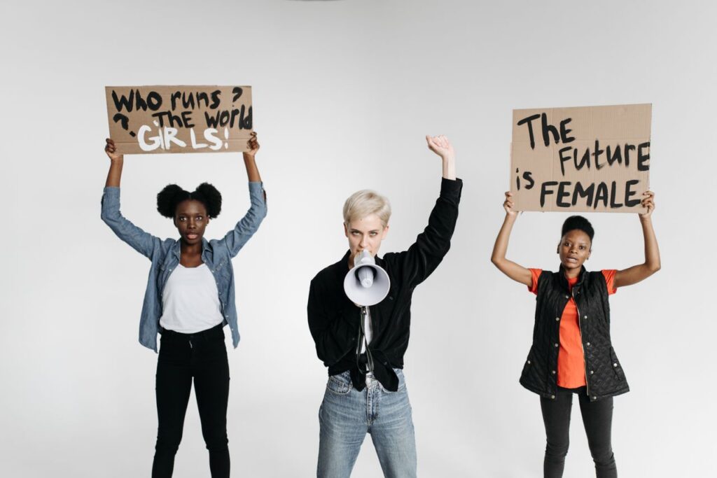 Three women holding protest signs and a megaphone advocating for women's rights in a studio setup.